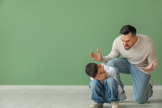 Angry father shouting at his crying son near green wall