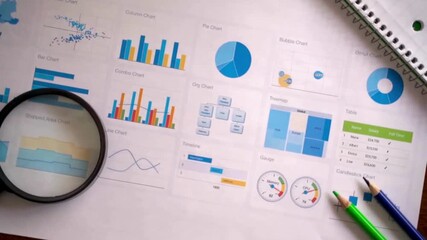 A visual display of various business charts, graphs (pie, bar, scatter), and tables on paper, accompanied by a magnifying glass, pencils, and a notebook. It emphasizes the process of data examination  - Powered by Adobe