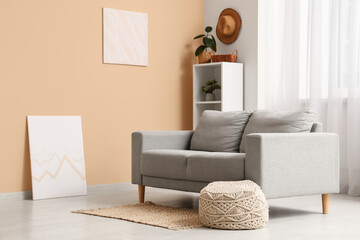 Interior of living room with comfortable sofa and pouf near beige wall