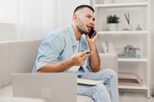 Young man talking on phone while planning work at home. Casual outfit and focused expression create a relatable atmosphere of productivity and modern lifestyle.