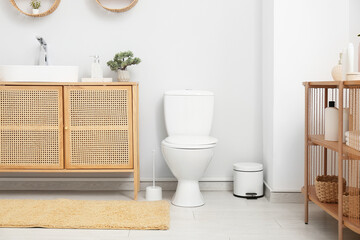 Interior of light restroom with toilet bowl, sink and bin