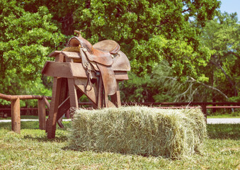 Leather horse saddle displayed on a wooden stand and a hay bale