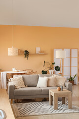 Interior of stylish living room with comfortable sofa, folding screen and table near beige wall