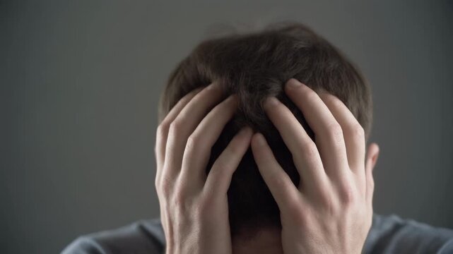 A person with hands covering their face, expressing feelings of despair, stress, or sadness in a somber setting.