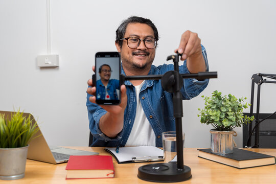 Man adjusting smartphone tripod while recording video content in creative home studio workspace