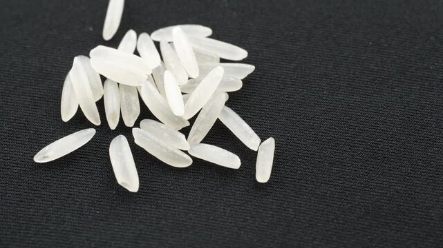 Top view 4K loop of a small pile of uncooked ST25 rice grains. The scene rotates slowly on a minimal black background. Conceptual video for premium food and agriculture.