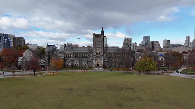 Cinematic moves inward from a distance over the historic University of Toronto campus, approaching University College, and revealing green back campus playing fields with the downtown Toronto skyline