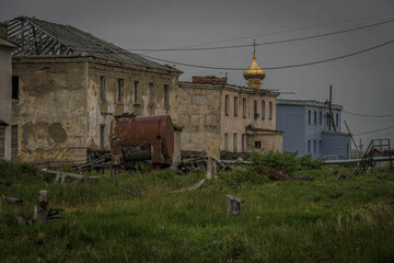 Fototapeta premium Orthodox dome rising above rusted tank and debris in Ugolnye Kopi, abandoned ghost town in Chukotka, Russia. 