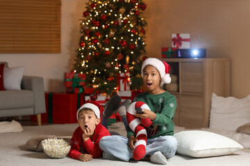 Surprised children in Santa hats with popcorn watching cartoons at home on Christmas eve
