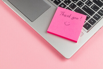 Thank you note on pink sticky pad next to laptop on a pink background © mykhailo