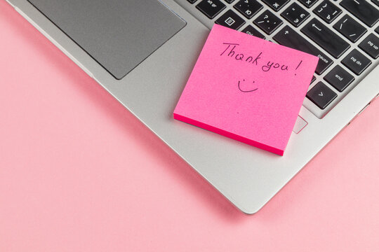 Thank you note on pink sticky pad next to laptop on a pink background