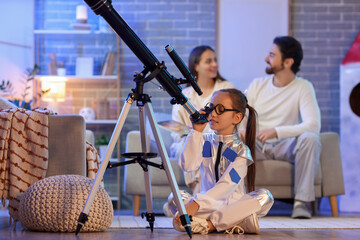 Little girl looking through telescope and her parents at home in evening