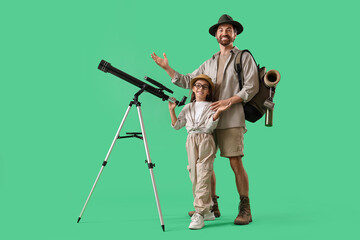 Fototapeta premium Male adventurer with his little daughter and telescope on green background