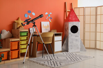 Fototapeta premium Interior of stylish children's room with cardboard rocket, table, toys and modern telescope