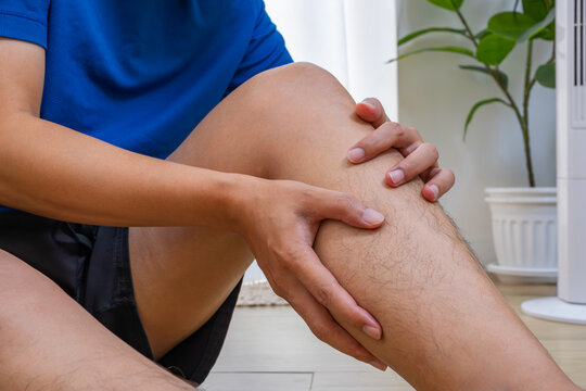 Person seated indoors, gripping painful calf with both hands. Calm home setting with copy space for medical care, muscle strain, or physiotherapy ads.