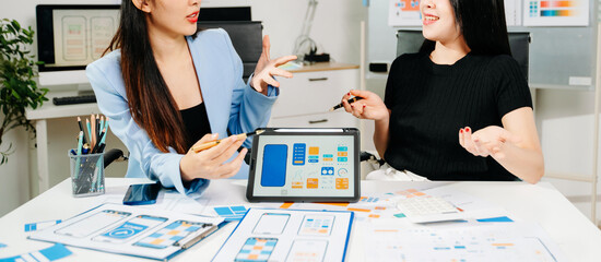 Two UX UI designers brainstorming mobile app wireframes in a modern startup office, showcasing creative teamwork, digital design