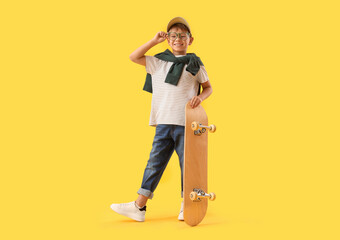 Little boy in eyeglasses with skateboard on yellow background © Pixel-Shot