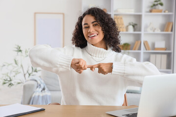 Young African-American woman using sign language near table at home