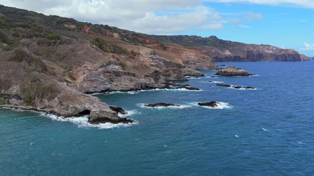 Drone pans across a rocky Hawaiian shore rarely seen by visitors, revealing epic cliff faces and turning to show the magnificent view of the island from the sea. 3 of sequence of 5.