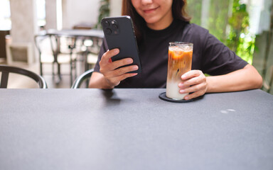 Closeup image of a woman holding and using mobile phone while drinking coffee in cafe