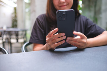 Closeup image of a woman holding and using mobile phone in cafe
