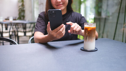 Closeup image of a woman holding and using mobile phone in cafe