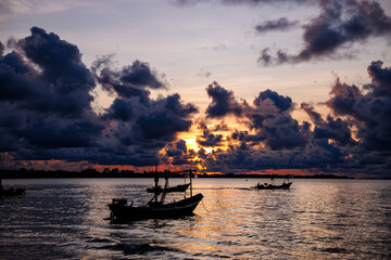 A silhouette of two fishing boats is set against the shimmering water as the sun dips behind...