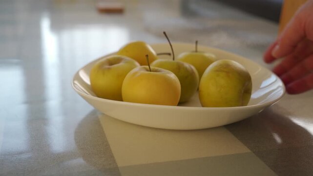 A ceramic bowl of apples is pushed across a tablecloth. This creates a soft scraping sound, and the apples rustle gently against each other.