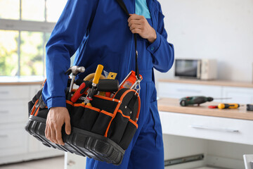 Male worker with tool bag assembling furniture in kitchen