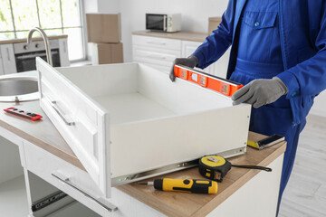 Male worker with level assembling drawer in kitchen