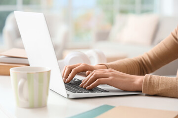 Fototapeta premium Female hands using laptop to search online on table at home, closeup