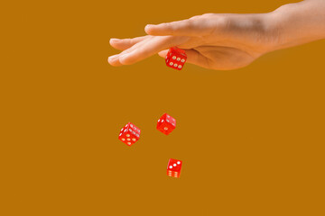 Female hand throwing game dices on orange background