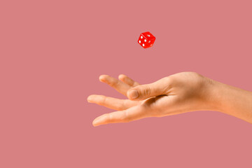 Female hand throwing game dice on pink background