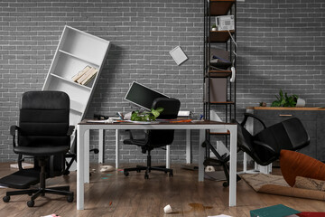 Interior of messy office with workplace and shelf units after earthquake