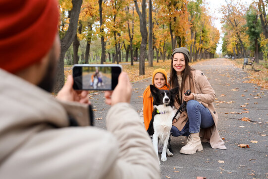 Young man taking picture of his family with dog in autumn park