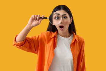 Shocked young woman with magnifier on yellow background. Search concept