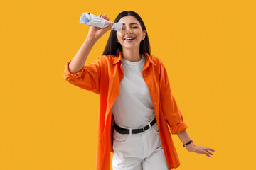Young woman looking through rolled newspaper on yellow background. Search concept