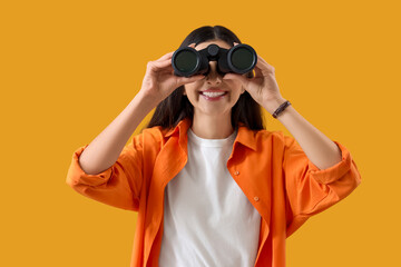 Young woman looking through binoculars on yellow background. Search concept