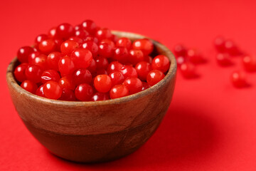 Wooden bowl with fresh viburnum berries on red background, closeup