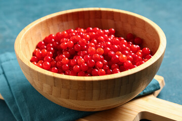 Wooden bowl with fresh viburnum berries on green background