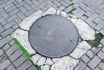 Gray Metal Manhole Cover on Cracked Brick Pavement with Green Moss Accents