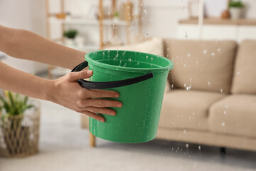 Female hands holding bucket under leaking water in living room. Flood concept © Pixel-Shot