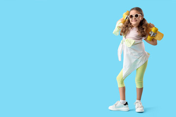 Cute little girl with skateboard and sunglasses on blue background