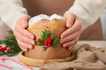 Female hands holding Panettone with Christmas decor on table at home, closeup