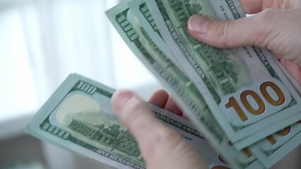 Hands of a woman counting one-hundred dollar bills to pay for expenses, symbolizing the high cost of living, rising inflation, and payment for expensive household utility bills