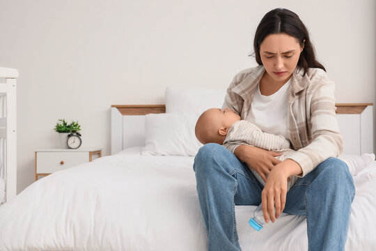 Young mother with bottle and her baby suffering from postnatal depression in bedroom - Powered by Adobe