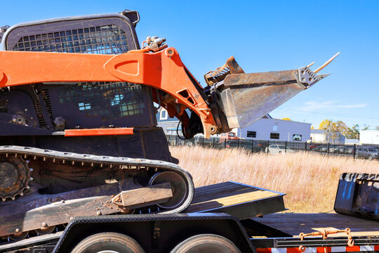 Skid steer machinery loader is positioned on flatbed trailer under its equipment.