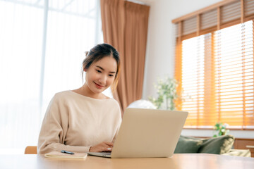 Beautiful young Asian woman working with laptop computer in living room. Work at home