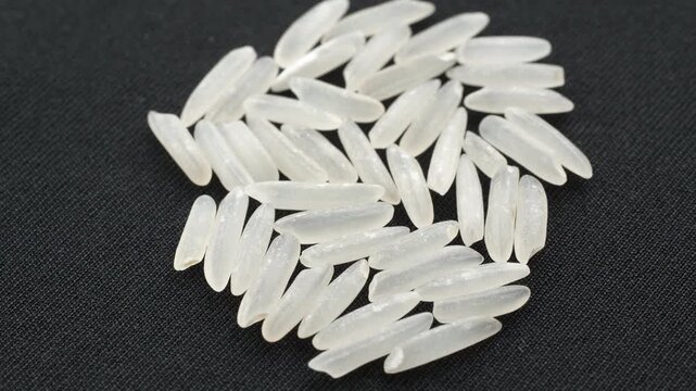 Top view 4K loop of a small pile of uncooked ST25 rice grains. The scene rotates slowly on a minimal black background. Conceptual video for premium food and agriculture.