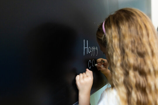 Young girl writing on chalkboard in classroom